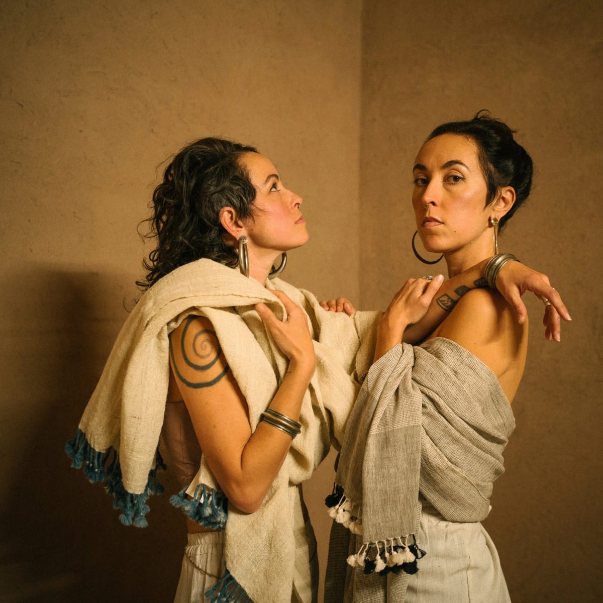 Leah Song and Chloe Smith of Rising Appalachia wrapped in handwoven shawls against an earthen wall